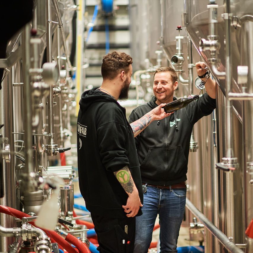 Lernender Brauer, Noah Peer, und Leiter Abfüllung, Thomas Voggesser, beim Tankkeller am Bier zapfen.