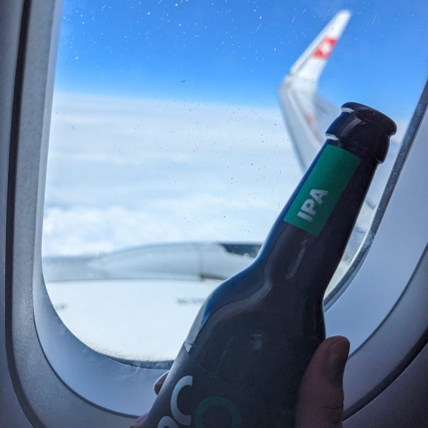 Cosmos IPA im SWISS Flugzeug vor dem Fenster, dahinter ein verschwommener Flugzeugflügel